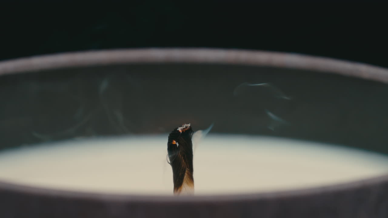 Close up macro of lit candle wick being blown out and smoking in slow motion