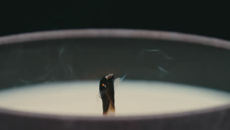 close up macro of lit candle wick being blown out and smoking in slow motion