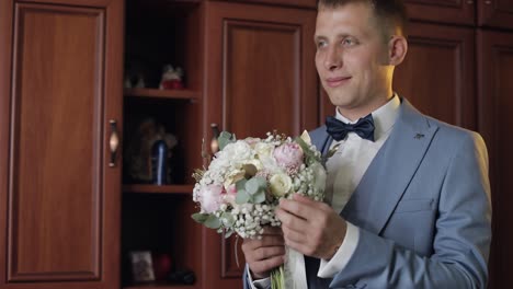 groom with wedding bouquet in his hands at home. white shirt, jacket