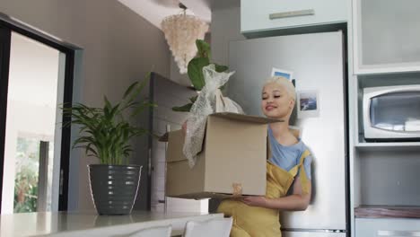 Happy-biracial-woman-walking-with-carton-with-plant-at-home-in-slow-motion