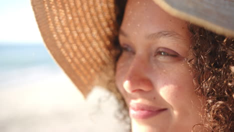 a young biracial woman wears a sunhat at the beach