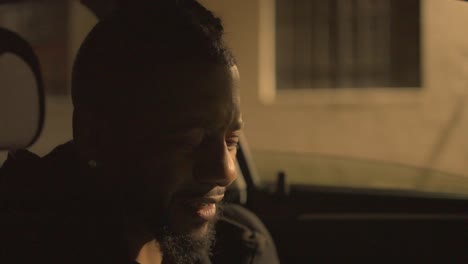 a black man sitting in a car outside a warehouse is experiencing regret