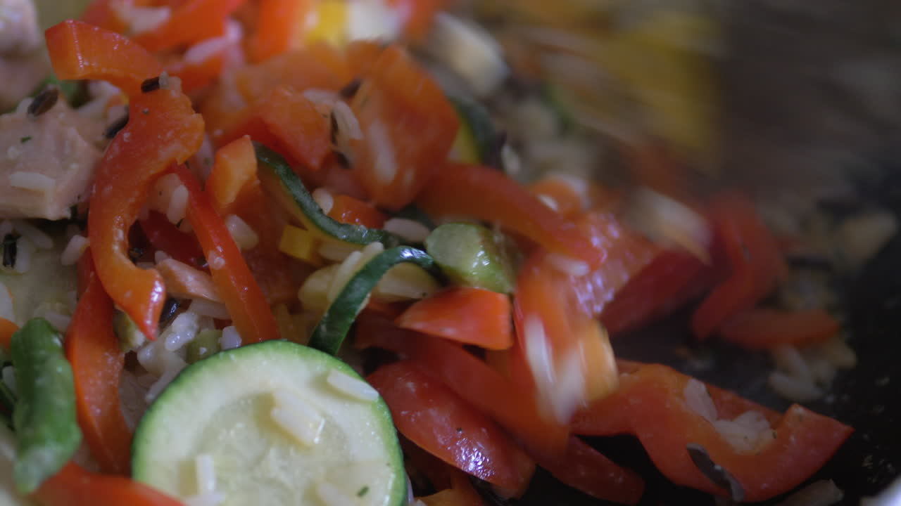 사람은 연어와 당근, 봄 양파와 같은 다양한 야채를 곁들인 볶음밥으로 팬을 요리하고 있습니다.