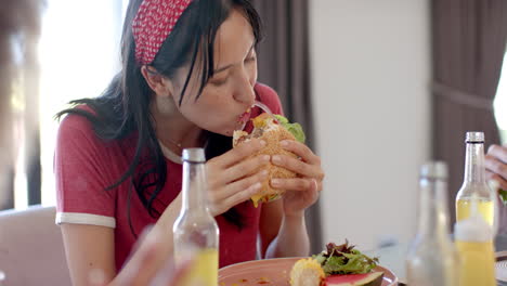 eating burger, woman enjoying meal with diverse friends at table, drinking juice
