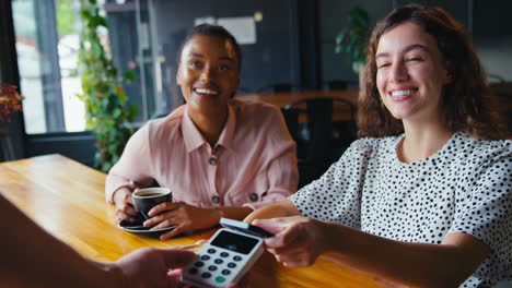 woman in coffee shop paying bill with contactless mobile phone payment