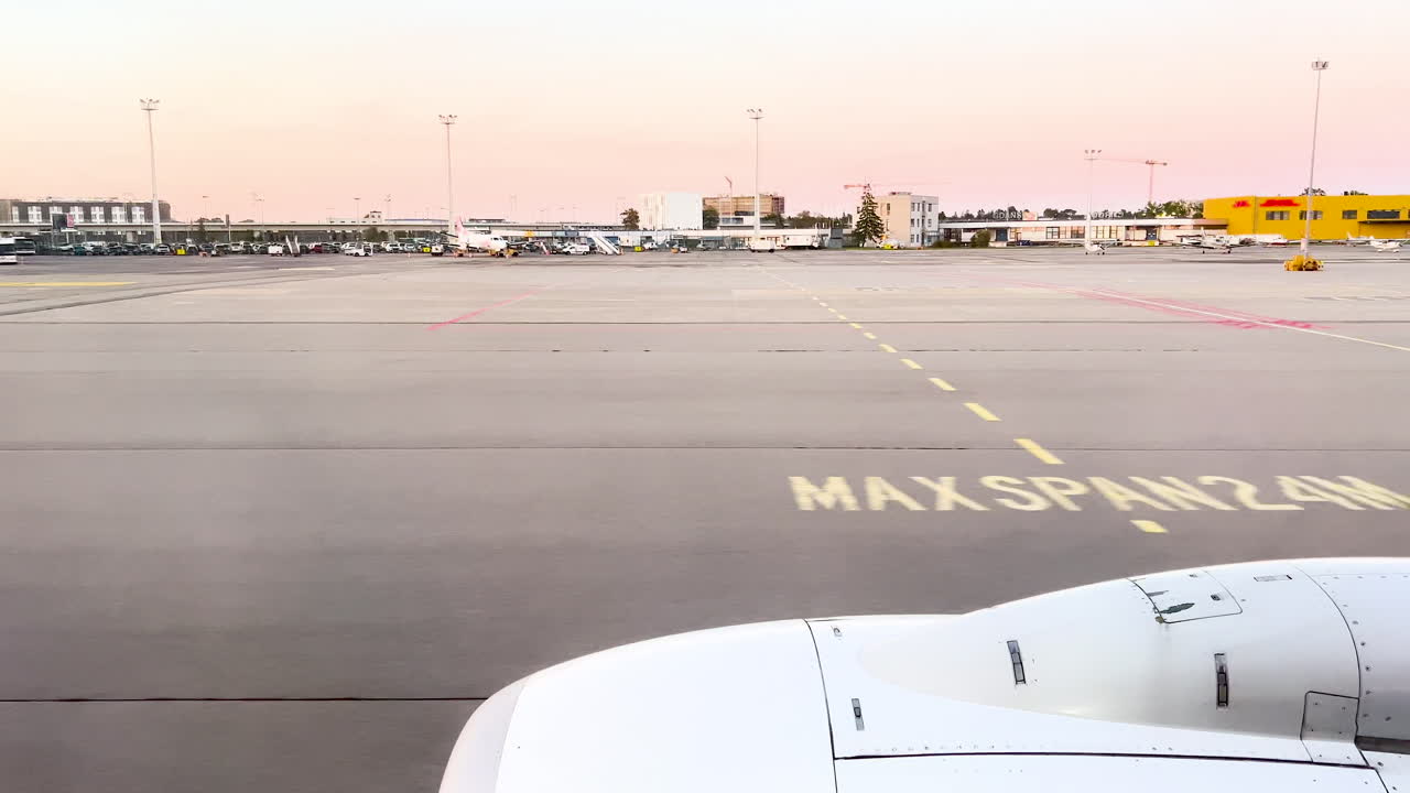 Sunset at airport with 'MAX SPAN 24M' marking on tarmac, airplane wing in view, and aircraft in the distance