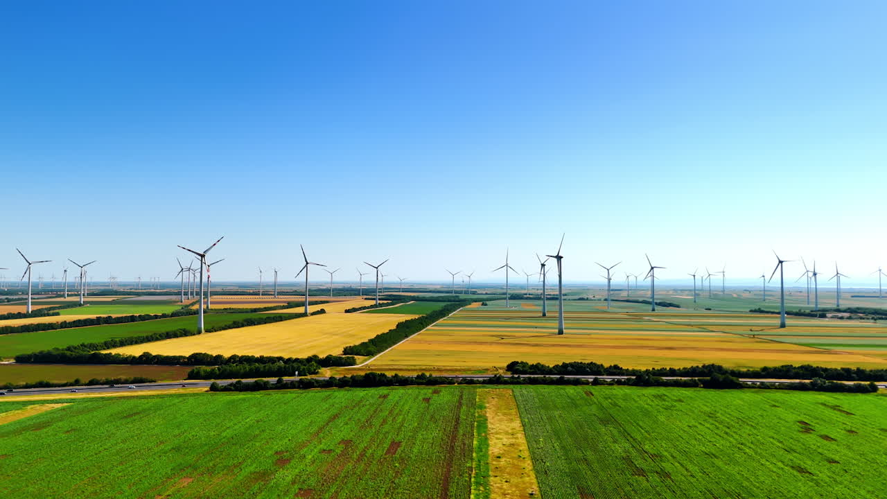 Flying over the green field approaching the fields with wind farms. Production of sustainable energy