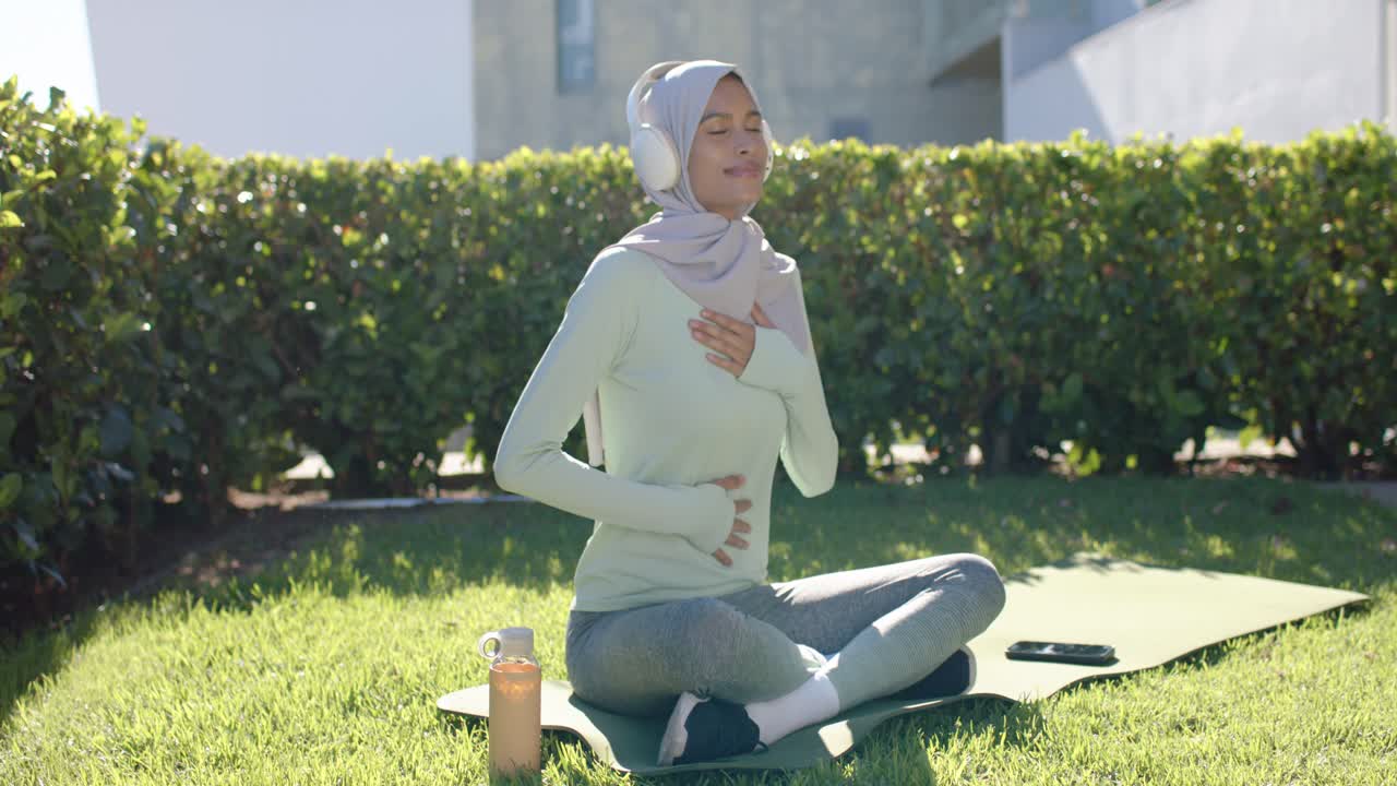 Wanita Afrika-Amerika bernapas di atas matras dengan tangan di dada, mendengarkan ponsel untuk ketenangan prenatal.