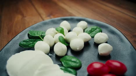 white small mozzarella cheese balls, spinach leaves and tomatoes on black plate. dolly-in shot