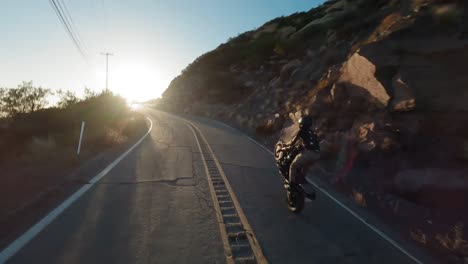 immersive fpv view from drone following stunt rider perfroming wheelie on asphalt winding road, topanga, california