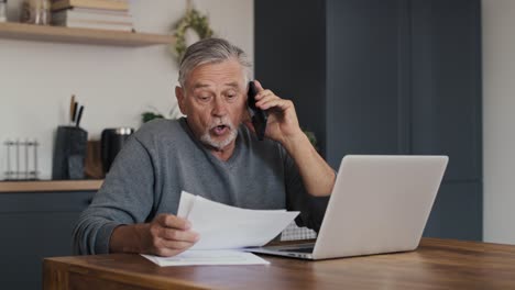 Shocked-caucasian-senior-man-looking-at-laptop-and-having-phone-call.