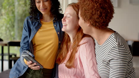 looking at smartphone, smiling female friends enjoying time together indoors