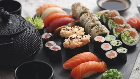 Assortment-of-different-kinds-of-sushi-rolls-placed-on-black-stone-board