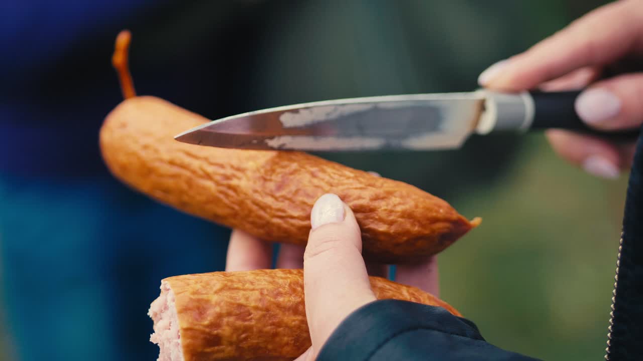 Woman makes cuts on a sausage with a knife