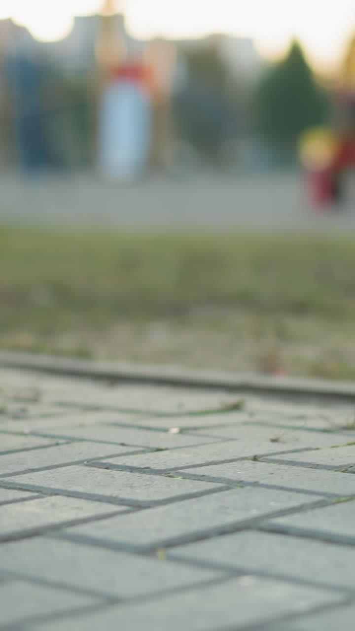 toma de primer plano centrándose en el intrincado patrón de ladrillos de piedra en un camino pavimentado del parque. el fondo es sutil como una pierna de banco de metal y pistas de un entorno de parque, incluyendo hierba y figuras distantes