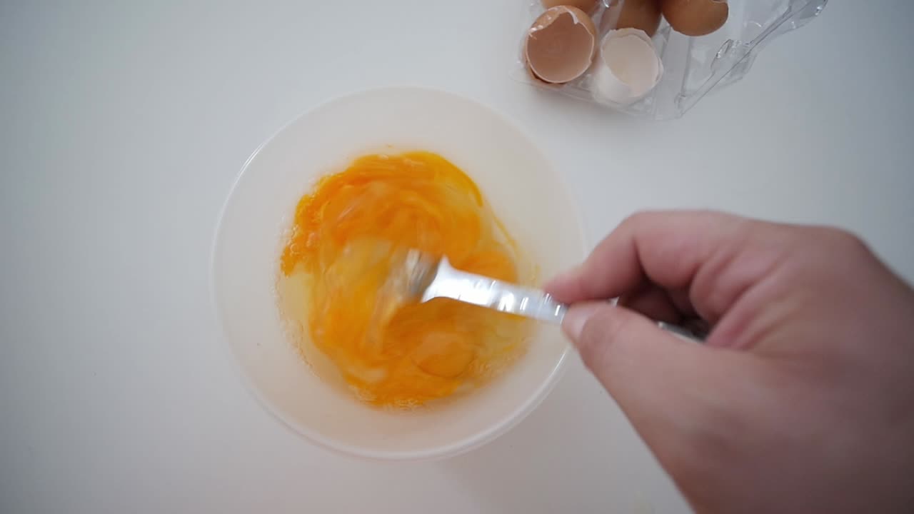 Whisking Egg Yolks With Fork In Bowl Top View With Broken Egg Shells In Background
