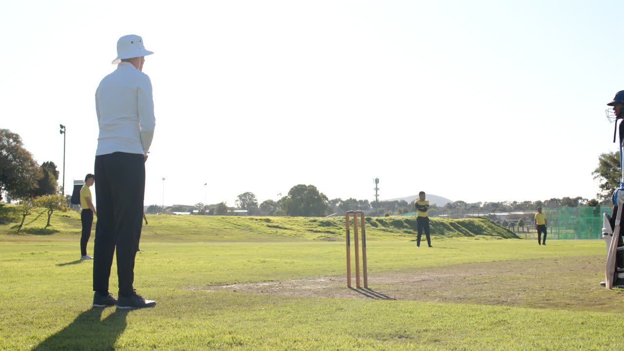 Cricket match in progress, bowler delivering ball to batsman on sunny field