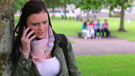 annoyed student leaning against a tree making a phone call