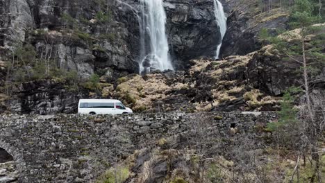 minibus passing bridge and famous waterfall hesjedalsfossen in slow motion, aerial norway