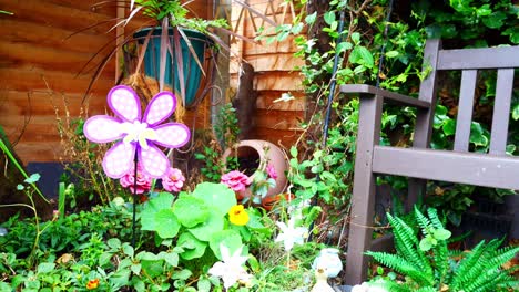 Colourful-spinning-childlike-butterfly-windmill-blowing-in-breeze-among-assortment-of-blossoming-flowers-and-plants