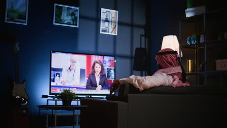 man lounged on sofa watching news