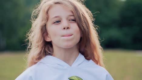 a little girl with long hair eats ice cream with a spoon from a cup. emotions of joy, delicious. child in the park in summer