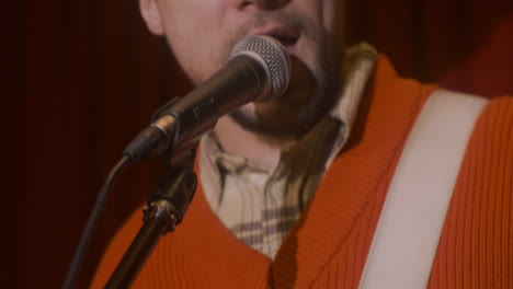 primo piano di un musicista maschio che suona la chitarra e canta durante la performance di musica dal vivo