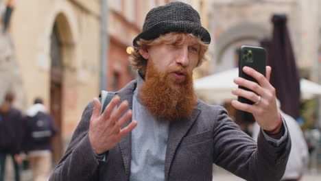 a man with a red beard talks on the phone on the street in the city