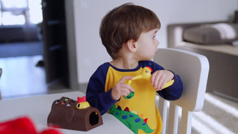 toddler boy sits at desk in his room. lovely baby playing with toys. blurred backdrop.