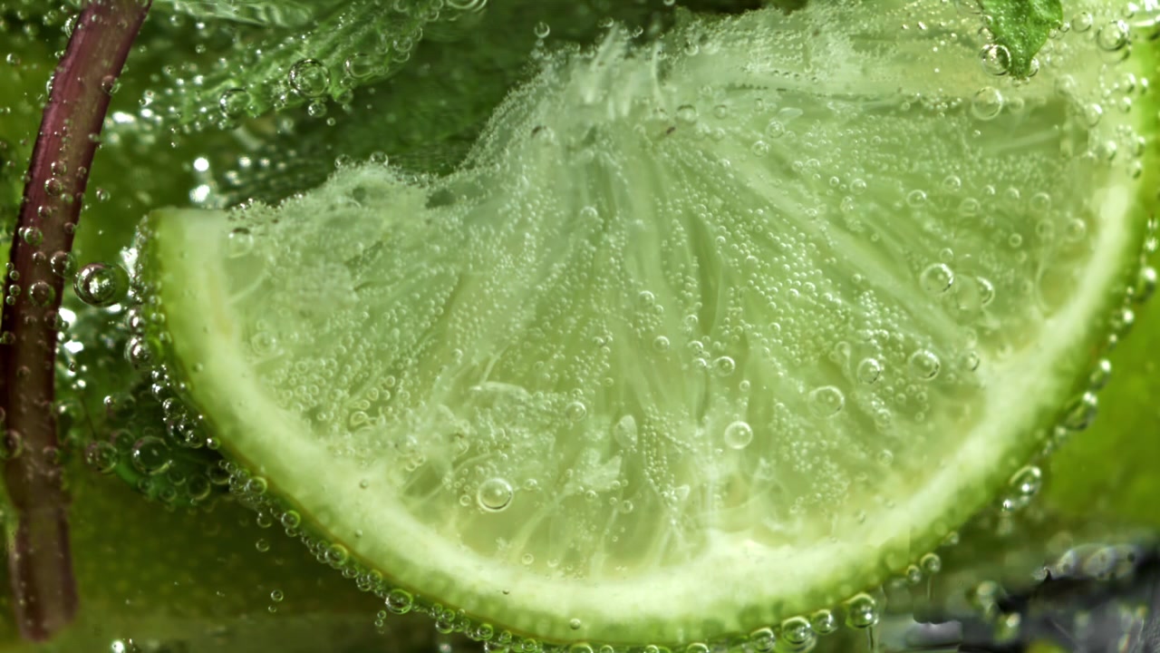 Fetta di lime vivace e foglie di menta in acqua frizzante con bollicine.
