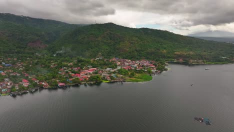 Pueblo-En-El-Lago-Taal-Frente-A-Montañas-Verdes-Durante-El-Día-Nublado