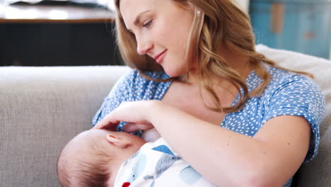 slow motion close up shot of mother sitting on sofa at home and breastfeeding baby