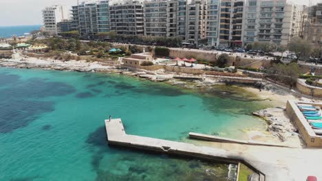 pier over the warm mediterranean sea on sliema's seaside, in malta - slow orbit aerial shot