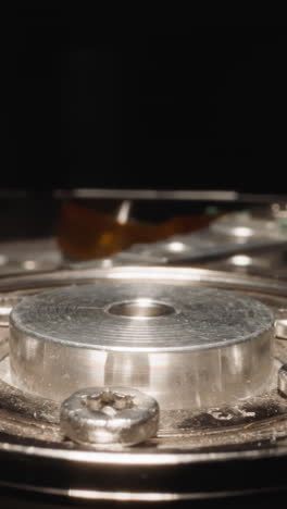open hdd with detailed mechanism reflecting bright studio light on dark background. electro-mechanical data storage device for computers macro