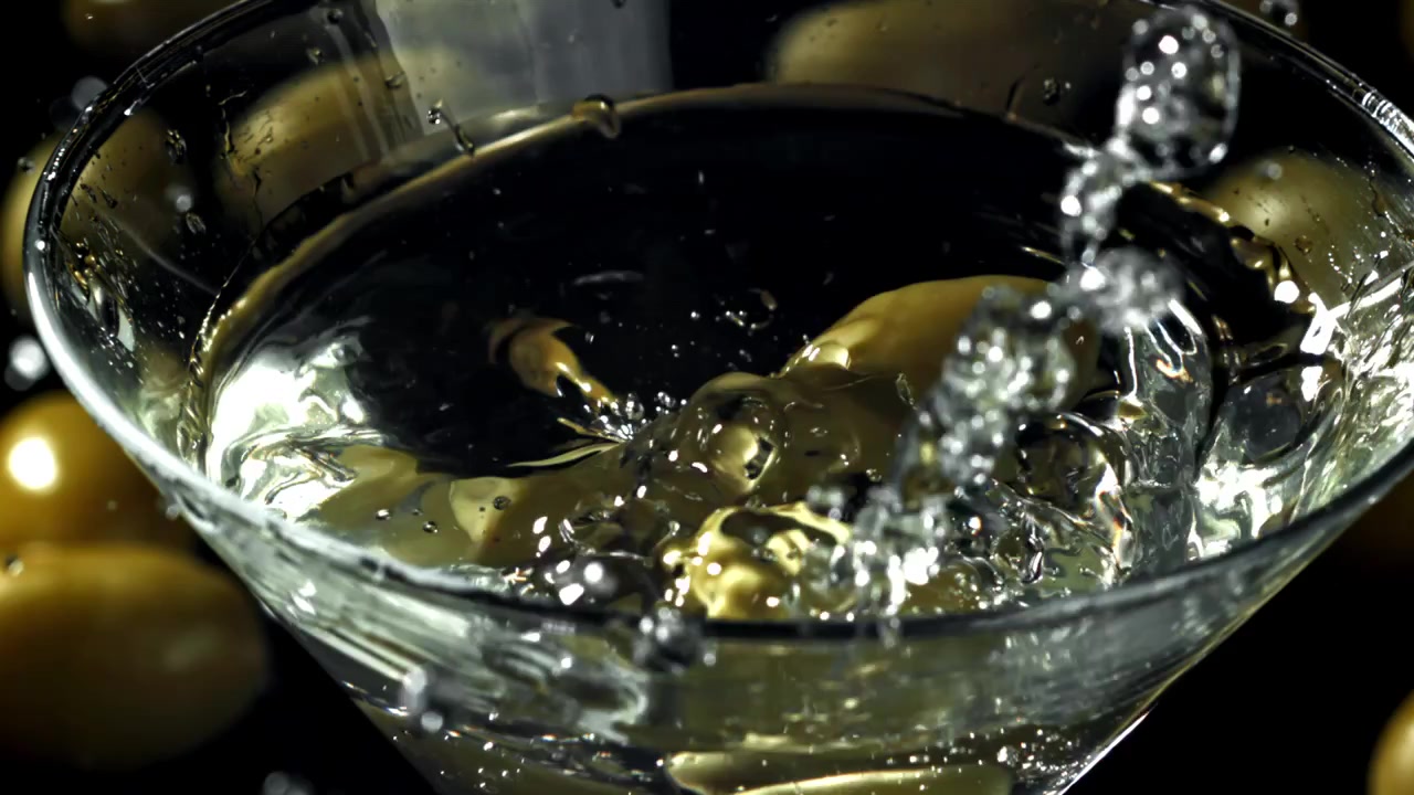 Olive verdi che cadono in un bicchiere da Martini al rallentatore