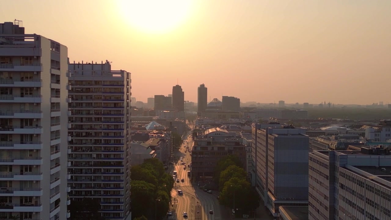 Edifícios de apartamentos na paisagem urbana de Berlim. Carros circulando por um bulevar ao pôr do sol, ladeado por árvores e edifícios de apartamentos, em uma paisagem urbana. Voo de drone em descida com vista aérea perfeita