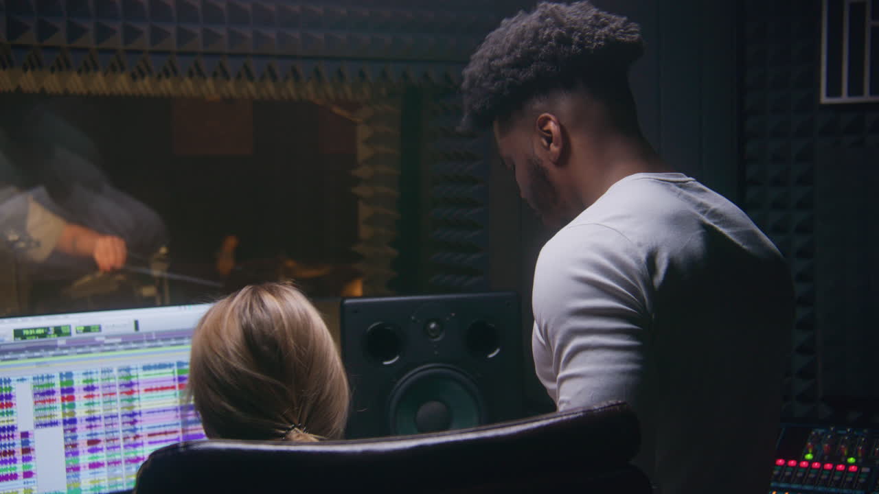 ingeniera de audio experimentada y productora afroamericana crean una nueva canción en el estudio de grabación de sonido. la vocalista canta la composición en el micrófono. la pantalla de la computadora muestra un programa profesional.