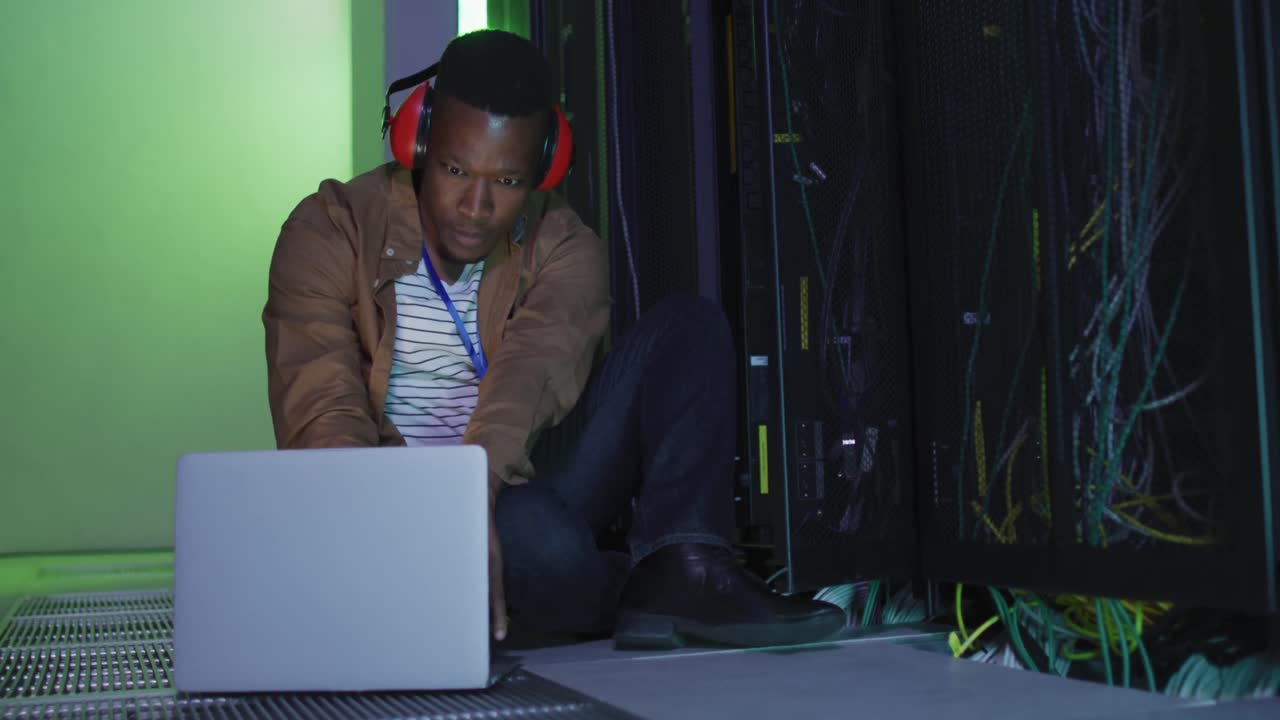 African american male computer technician using laptop working in business server room