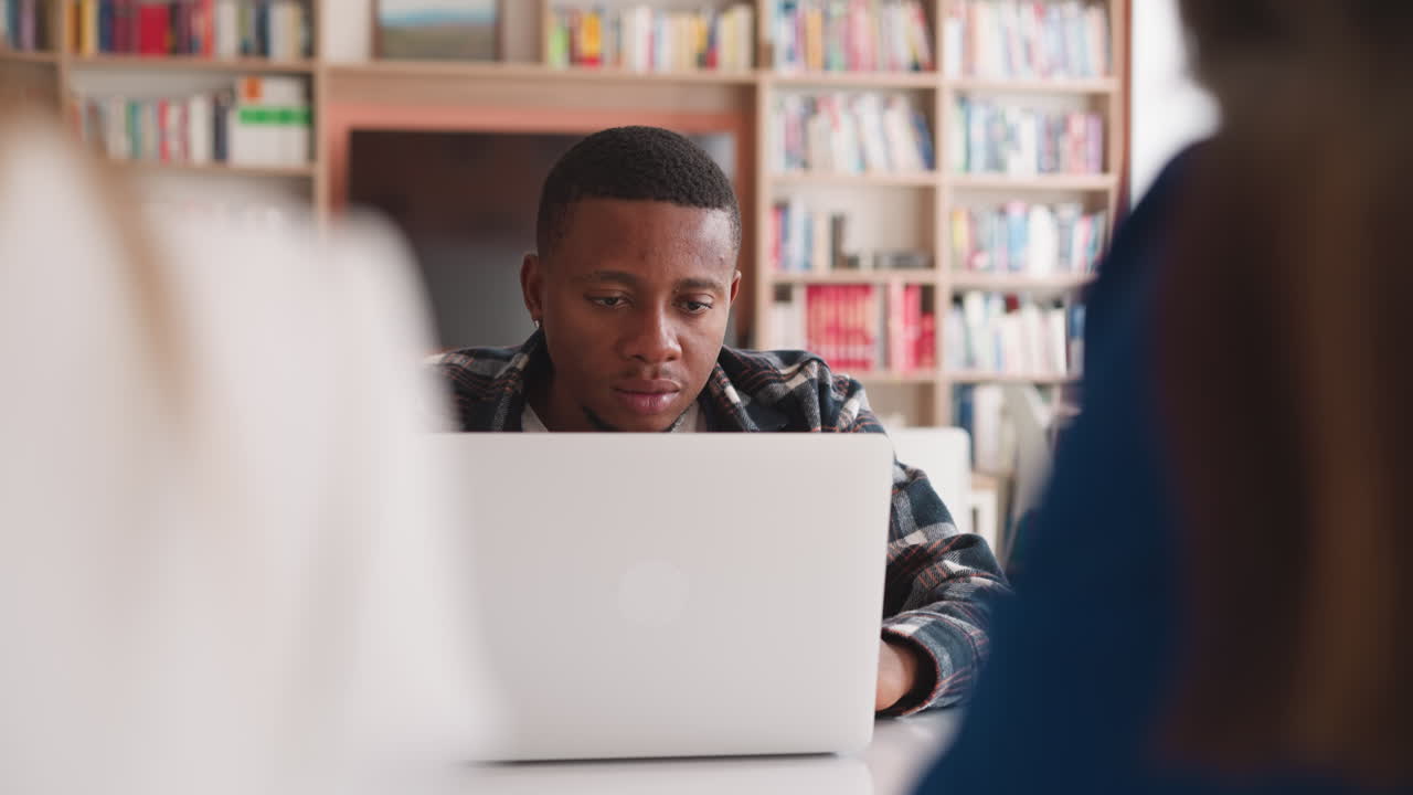 hombre con compañeras de grupo femeninas escriben un proyecto de investigación usando una computadora portátil. los estudiantes escriben investigando en la biblioteca usando dispositivos modernos. aprendiendo con tecnología moderna