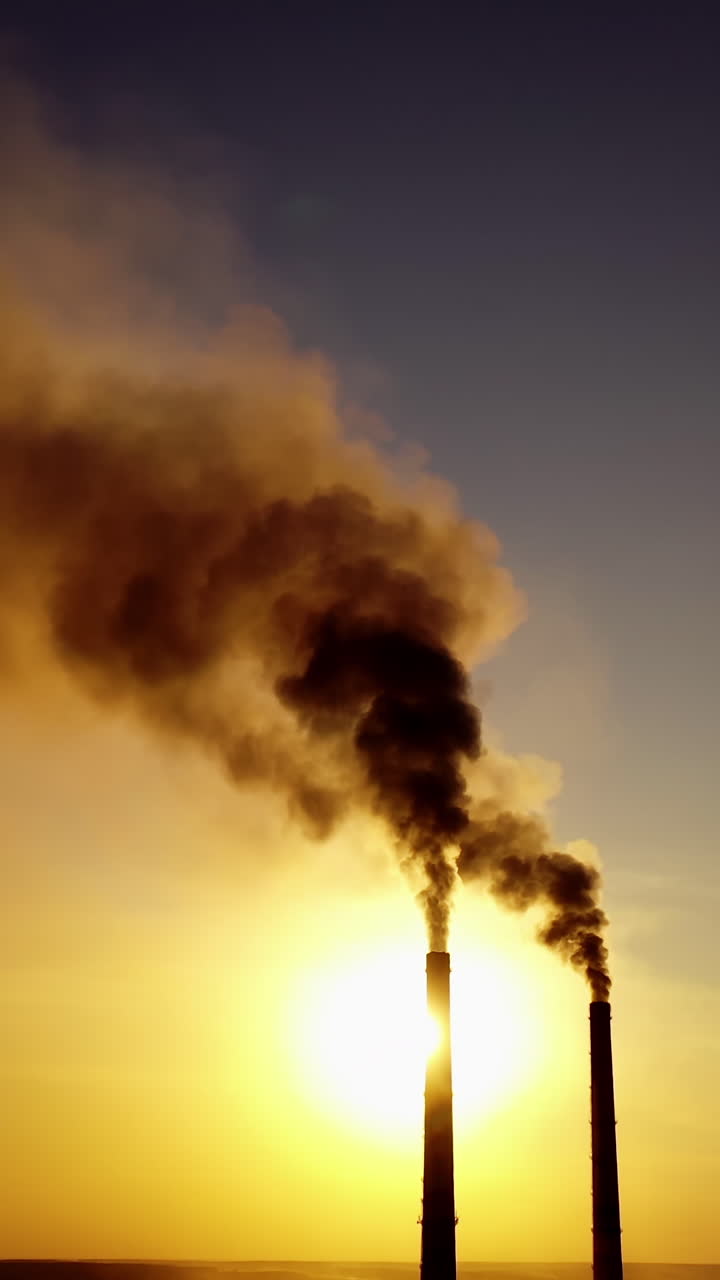 View of pipes with smoke. Power plant silhouette at sunset. Vertical video
