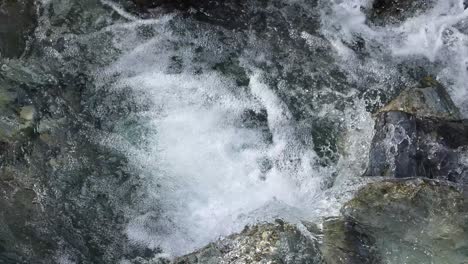 clear mountain stream water rushes over jagged rocks in daylight, captured from above with a steady camera, highlighting natural textures and dynamic movement