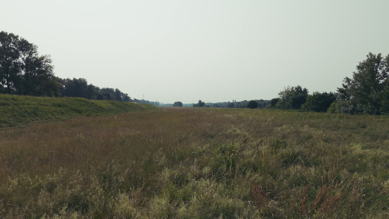 dry grassy field with levee embankments and distant tree line outside Zagreb under soft light