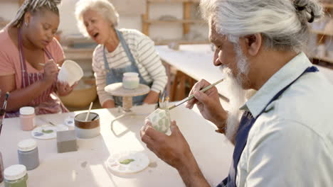 Happy-diverse-group-of-potters-glazing-clay-jugs-and-discussing-in-pottery-studio