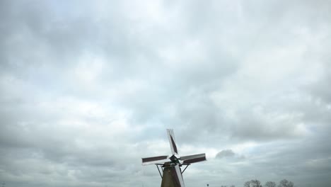 Windmills-turning-in-Dutch-fields-on-cloudy-day,-camera-tilt-down-reveal