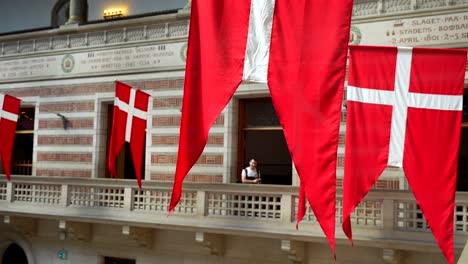 Un-Turista-Masculino-Posa-Detrás-De-Banderas-Rojas-Danesas-En-El-Ayuntamiento-De-Copenhague