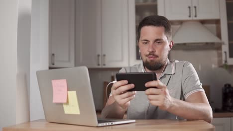 hombre usando teléfono inteligente y portátil en la cocina