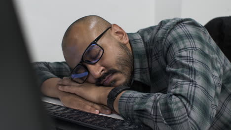 a young indian entrepreneur slumped over an office desk, asleep in front of his computer exhausted from working late putting together his business proposal