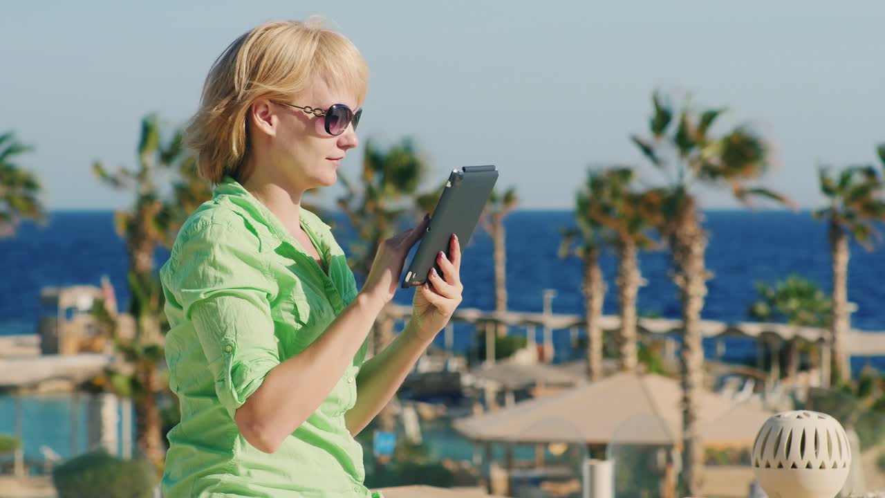 un turista con gafas de sol disfruta de la tableta en el fondo de un paisaje tropical