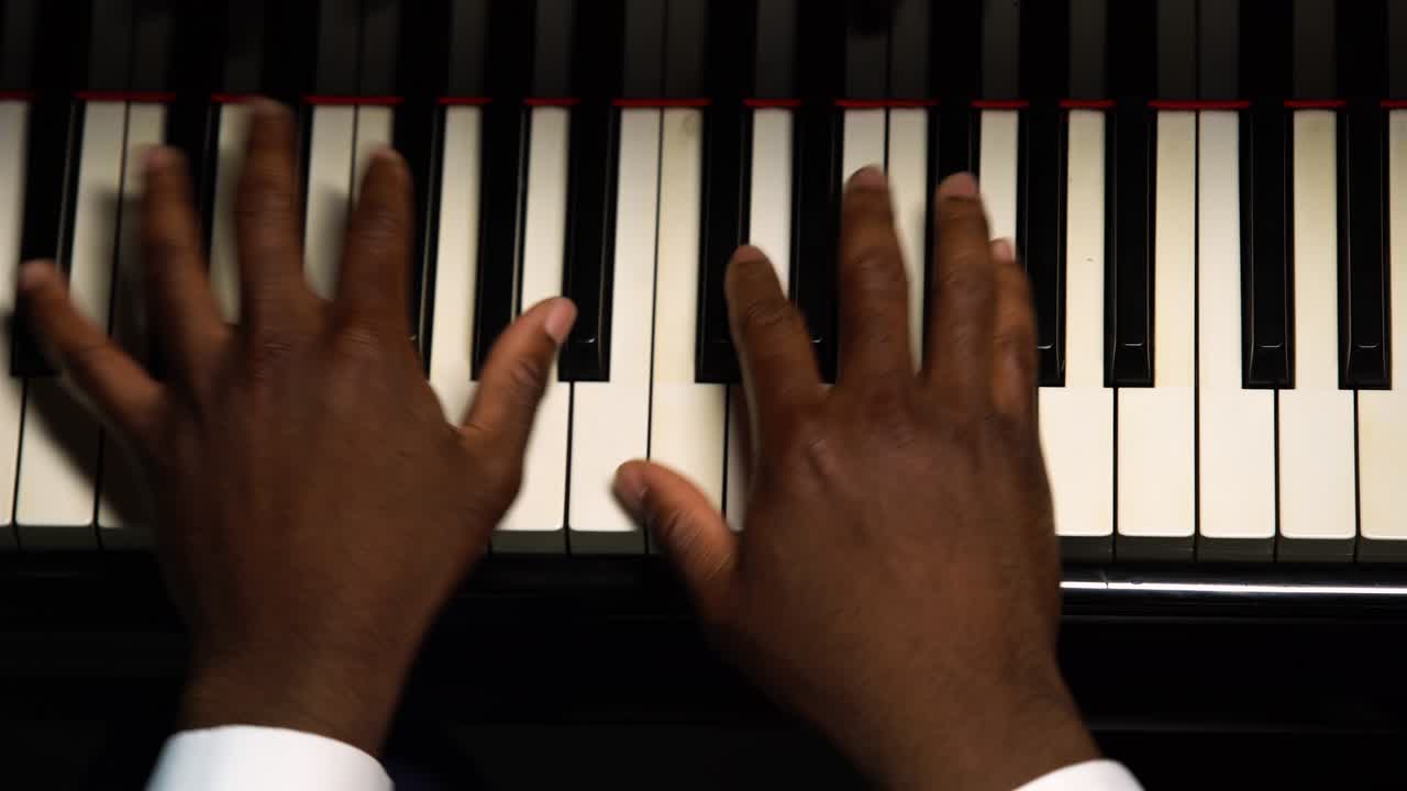 Top view of male hands playing the grand piano. The African American touches the black and white keys with his fingers to create the rhythm of the melody. Close up black hands of a male pianist