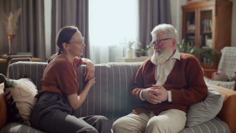 young woman chatting with senior grandfather on couch in living room